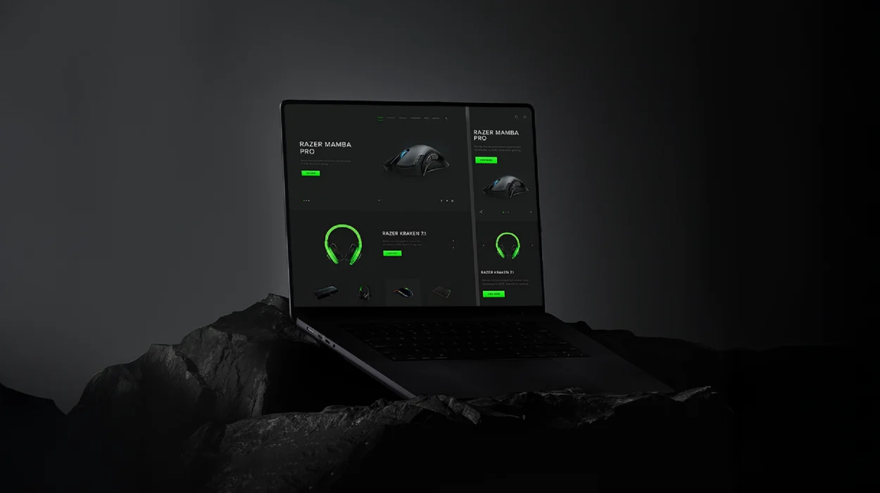 Dark-theme eCommerce website mockup on a laptop featuring Razer gaming products — including the Razer Mamba Pro mouse and Razer Kraken 7.1 headset — showcased on a rocky black background.
