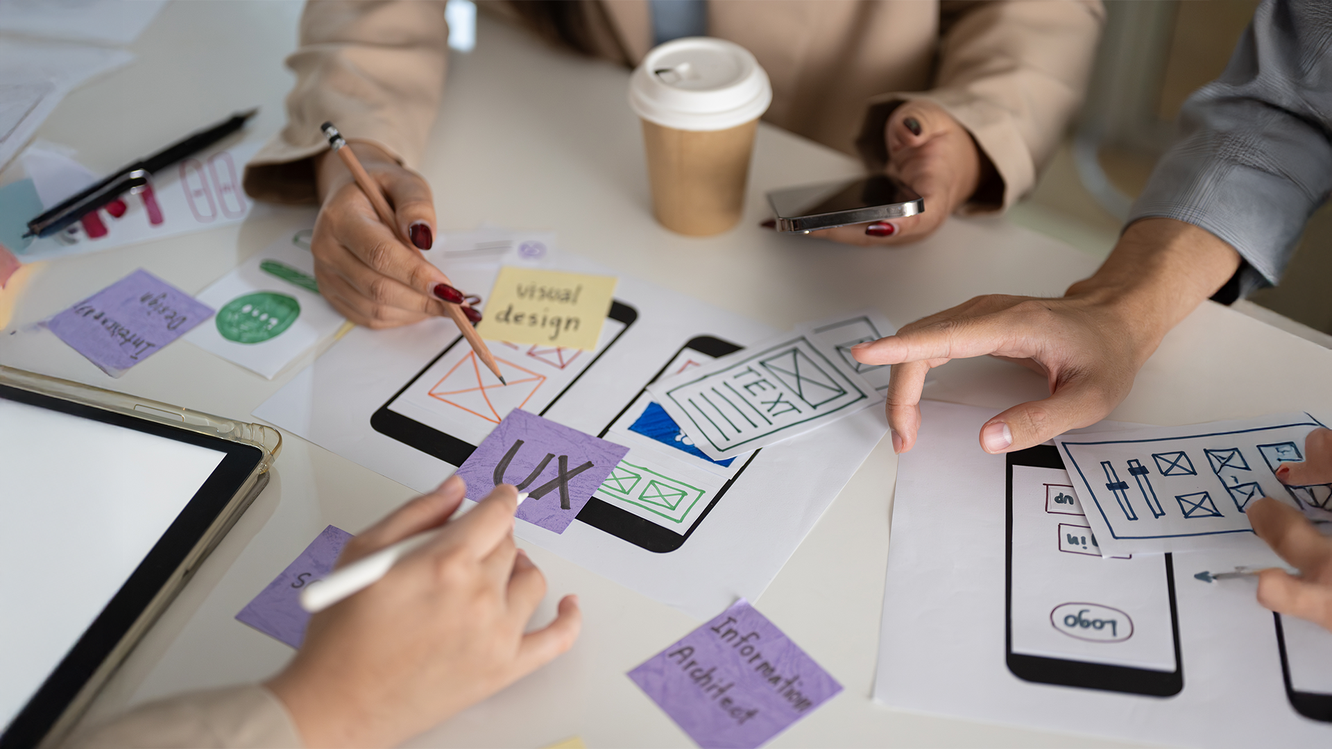 Creative UX design team brainstorming app wireframes with sketches, sticky notes, and digital tablets during a user experience planning session.