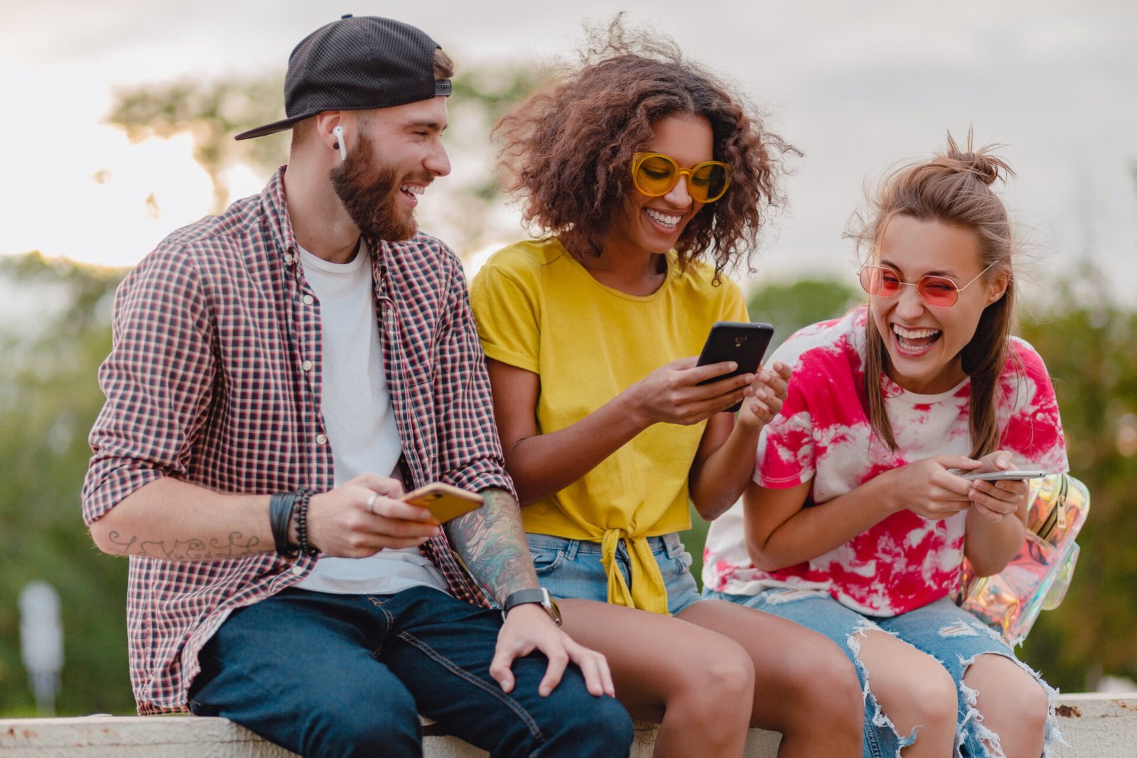 happy young company of smiling friends sitting park using smartphones, man and women having fun together, colorful summer hipster fashion style, communication wireless connecting devices